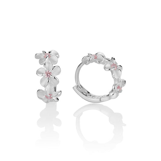The picture shows a pair of matte finish sterling silver plumeria hoop earrings with pink cubic zirconia. 