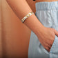 The photo shows a model wearing a yellow and white gold vermeil bangle with a tropical motif. 