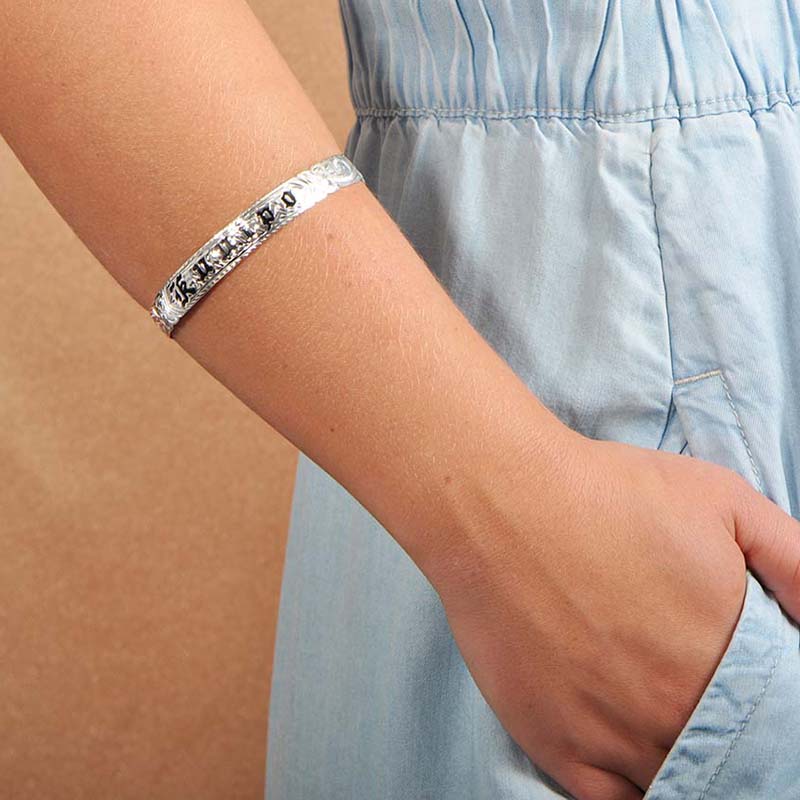 Model wearing a 10mm sterling silver bangle with the Hawaiian word "ku'uipo" engraved on it. 
