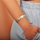 The photo shows the arm of a model wearing a two-tone white and yellow gold vermeil flowering plumeria cuff bangle. 