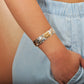 The photo shows the arm of a model wearing a two-tone white and yellow gold vermeil flowering plumeria cuff bangle. 