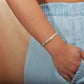 The photo shows the arm of a model wearing a two-tone white and yellow gold vermeil flowering plumeria cuff bangle. 