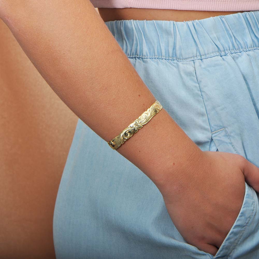 The photo shows the arm of a model wearing a yellow gold vermeil flowering plumeria cuff bangle. 
