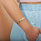 The photo shows the arm of a model wearing a yellow gold vermeil flowering plumeria cuff bangle. 