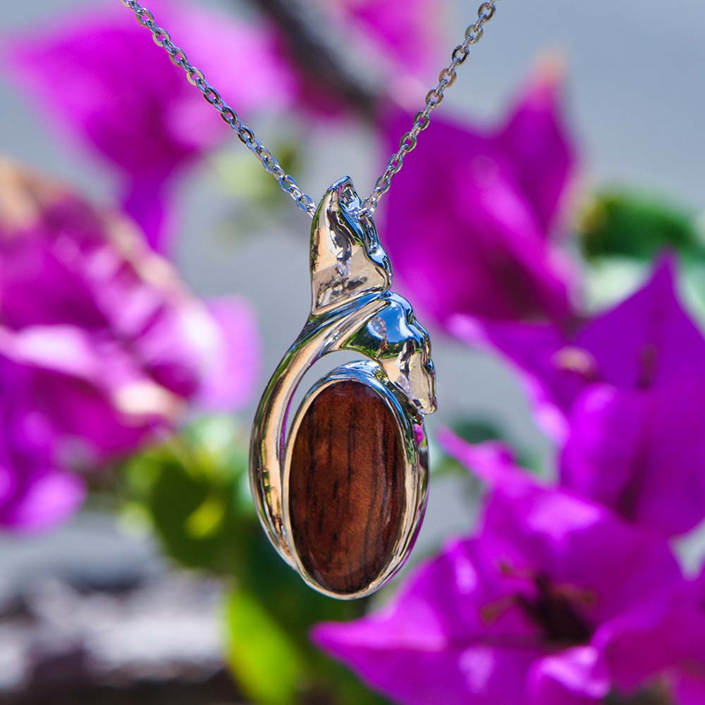 Koa wood oval pendnat with a sterling silver rim featuring a whale tale. 
