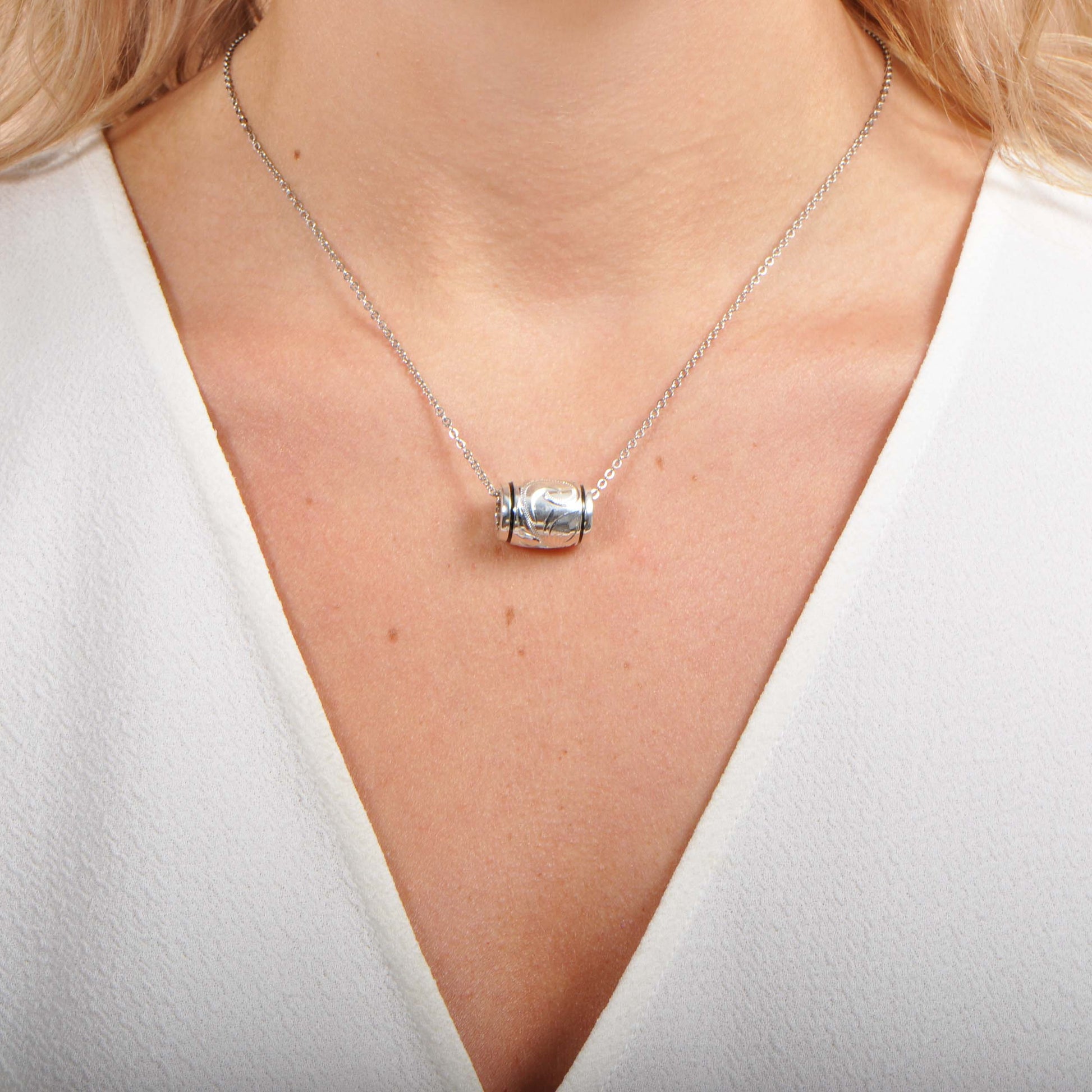 The photo shows a model wearing a silver barrel Hawaiian scroll design pendant. 