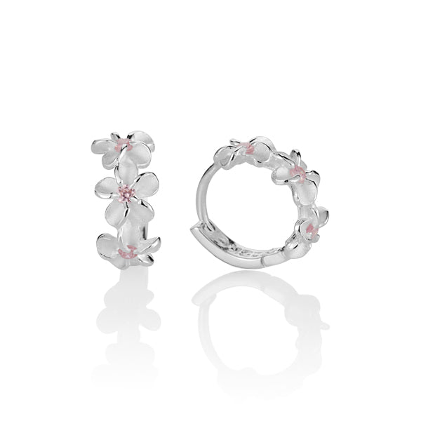 The picture shows a pair of matte finish sterling silver plumeria hoop earrings with pink cubic zirconia. 