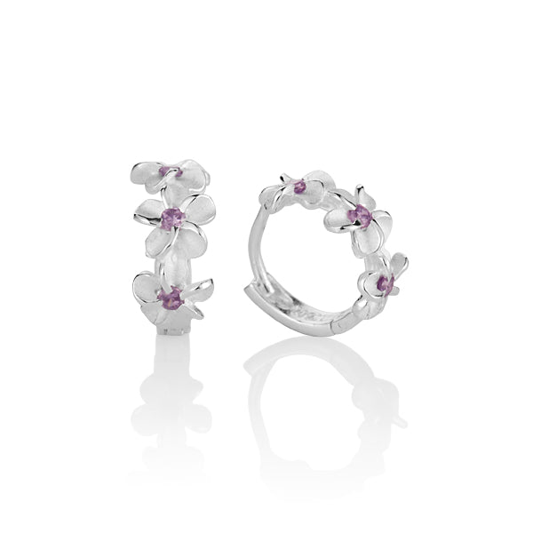 The photo is a pair of matte finish sterling silver plumeria hoop earrings with purple cubic zirconia. 