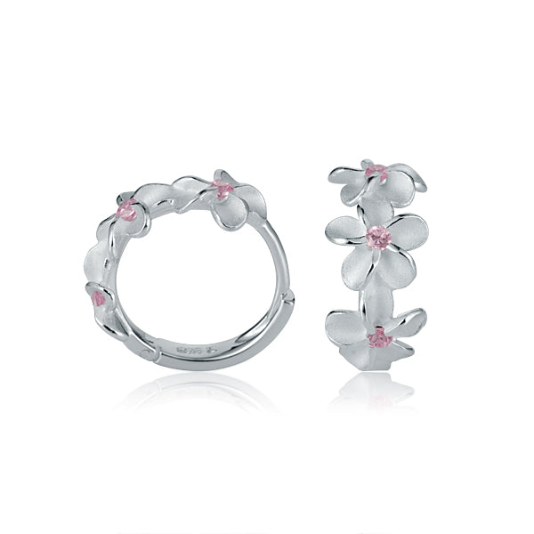 The picture shows a pair of matte finish sterling silver plumeria hoop earrings with pink cubic zirconia.