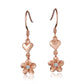 The photo shows a pair of rose gold vermeil heart hook earrings featuring a plumeria design with cubic zirconia. 