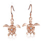 The photo shows a pair of rose gold vermeil sea turtle hook earrings featuring a plumeria flower with a cubic zirconia gem. 