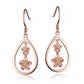 The photo shows a pair of rose gold vermeil plumeria hook earrings featuring a teardrop design with cubic zirconia. 