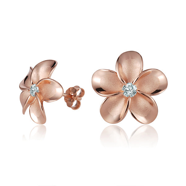 The photo shows a pair of rose gold vermeil plumeria stud earrings with cubic zirconia gemstones.