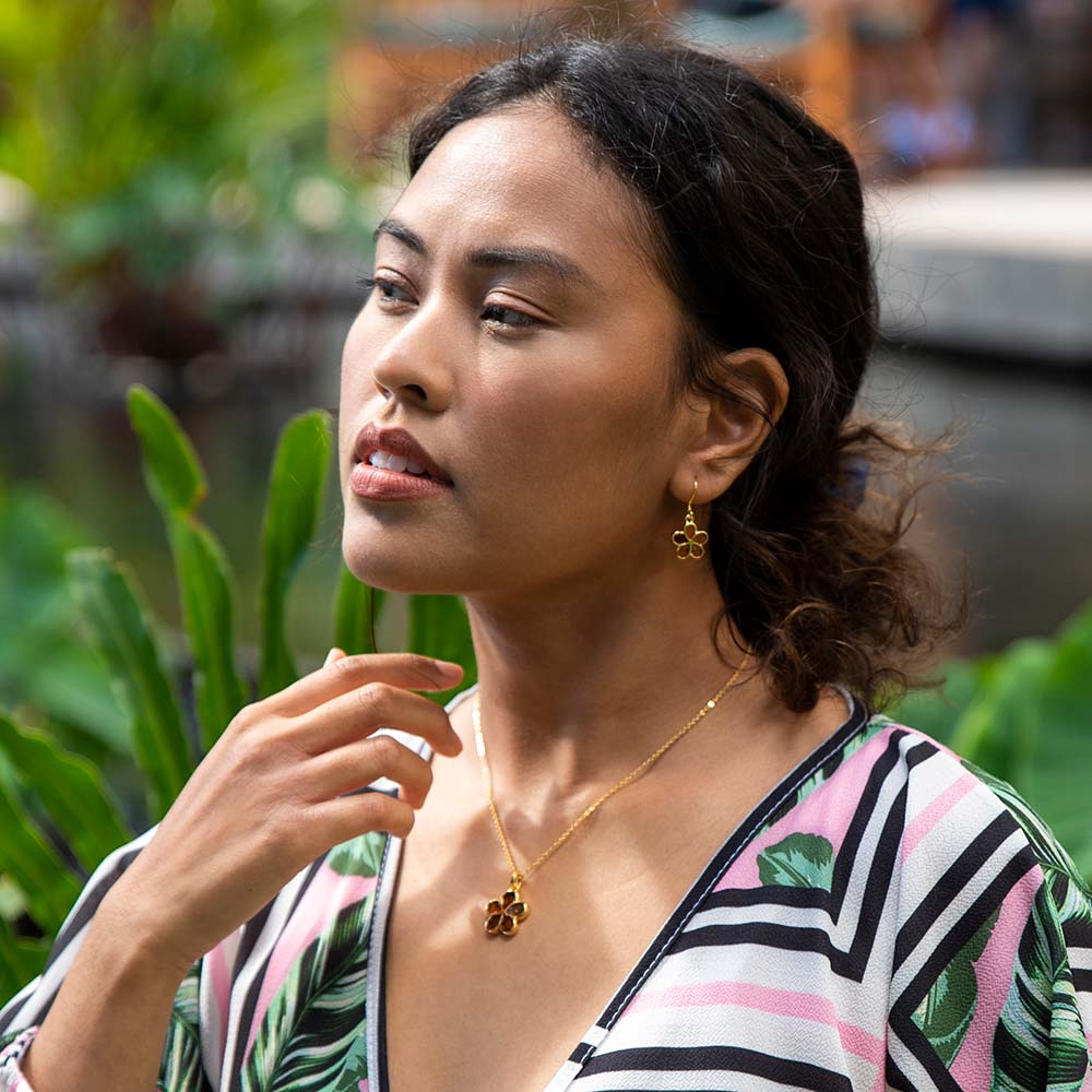 A model wearing a set of 14K gold vermeil and Koa wood earrings and pendant. The det is designed to look like a plumeria flower.